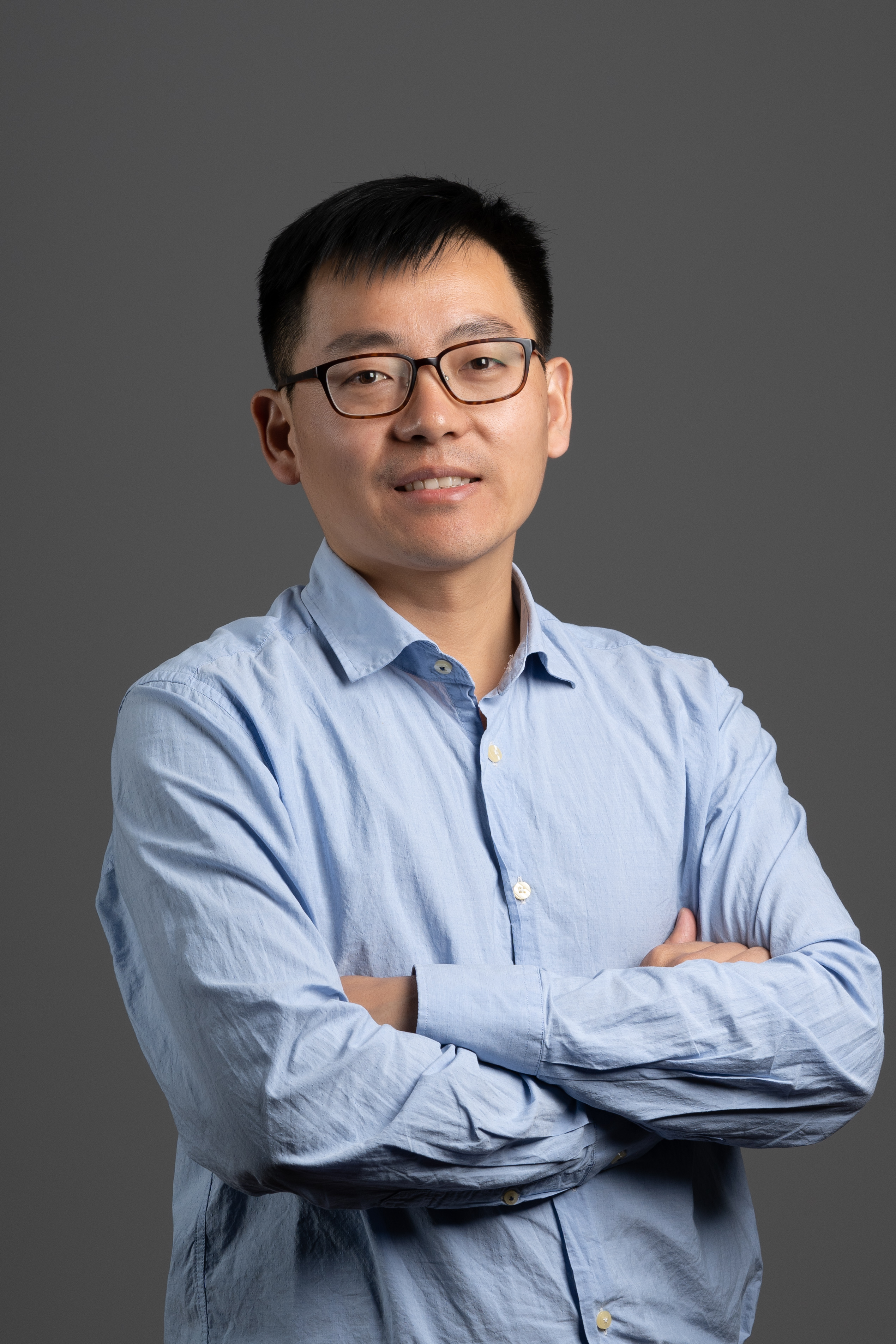 Liang Ma poses with crossed arms in front of grey background