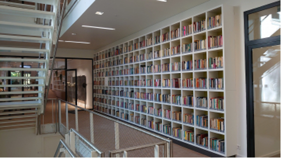 Photograph of the Bruner Library shows white bookshelf stacked with books and a staircase leading upwards