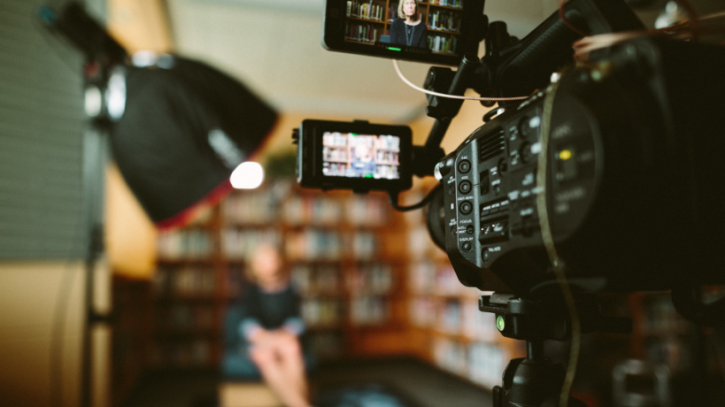 Stockphoto of a video camera recording a person sitting infront of a bookcase