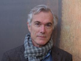 Timothy Brook, wearing a jacket and a scarf, standing in front of a painted background