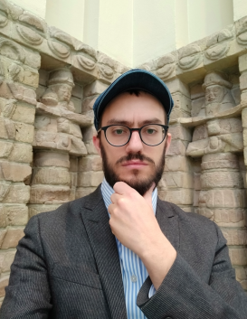 Yehuda Halper standing in front of a building, his left hand on his chin