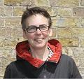 Christina Benninghaus (wearing a black and red jacket, glasses and short hair) posing in front of a brick wall