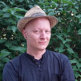 Sascha Topp, wearing a hat, posing in front of a tree